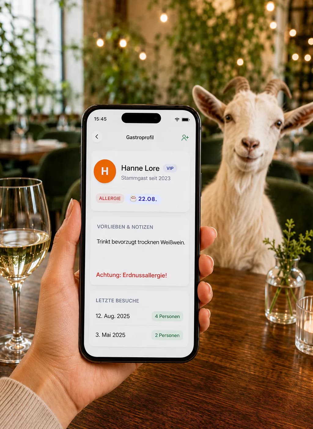 Smartphone zeigt ein digitales Gästeprofil mit Stammgast-, Allergie- und Besuchsdaten im Bringmal Tischreservierungssystem; daneben sitzt eine Ziege im Restaurant